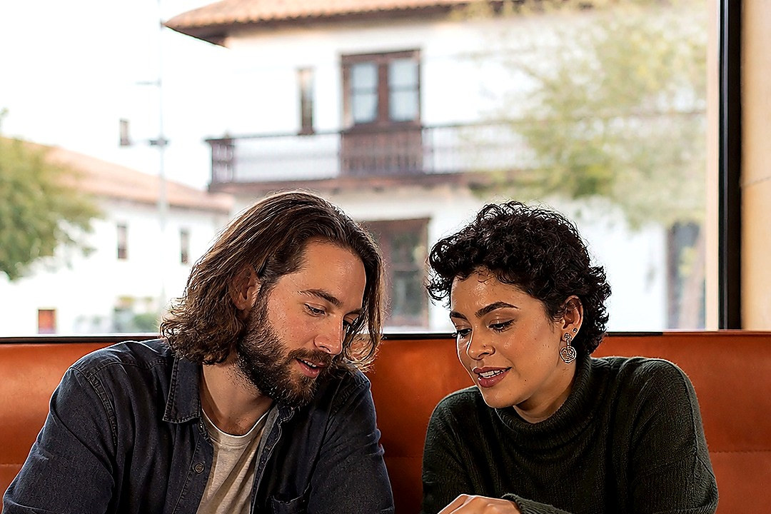 Two women sharing a phone during a relaxed café conversation.