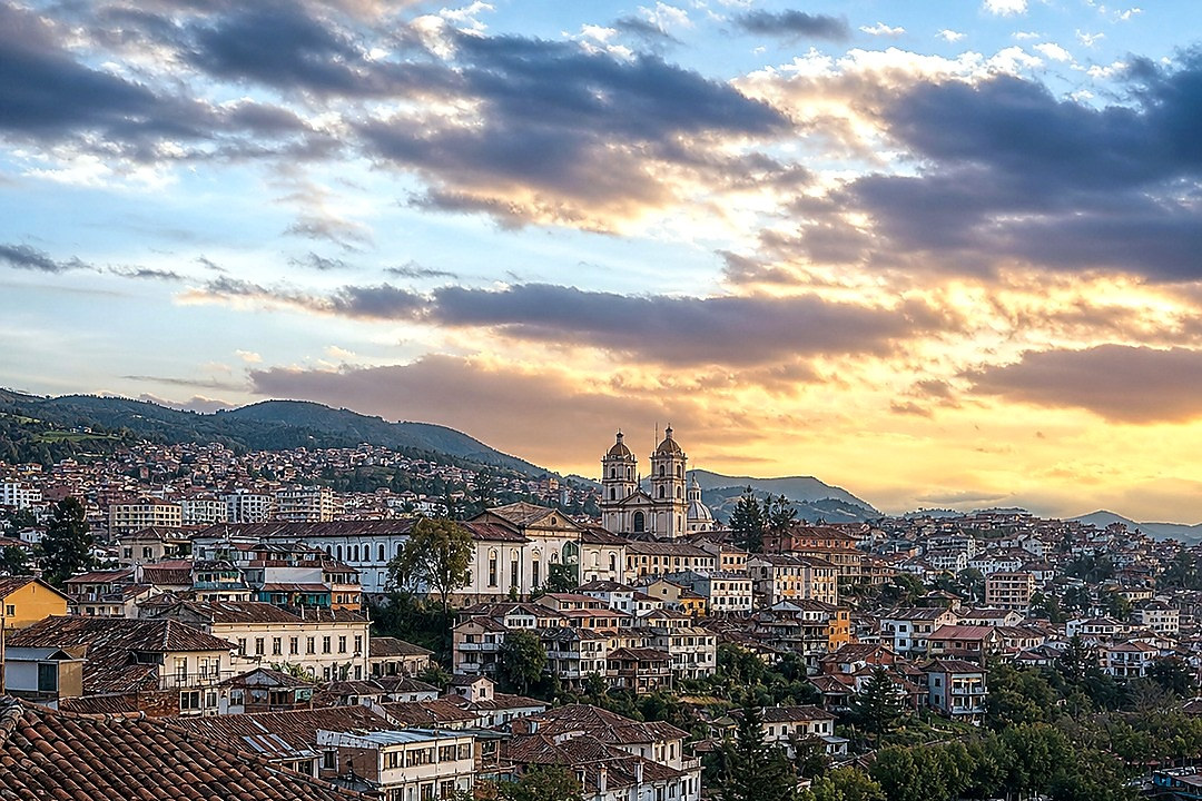 Colorful hillside neighborhoods and a historic church in Cuenca beneath a dramatic evening sky.