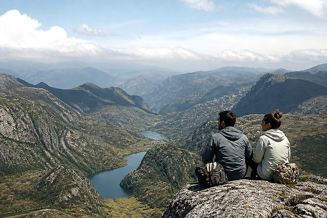 Two hikers seated on a rocky overlook above a deep forested canyon.